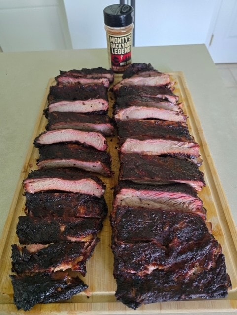 Two full racks of sliced BBQ ribs on a cutting board with Monty's Backyard Legend rub